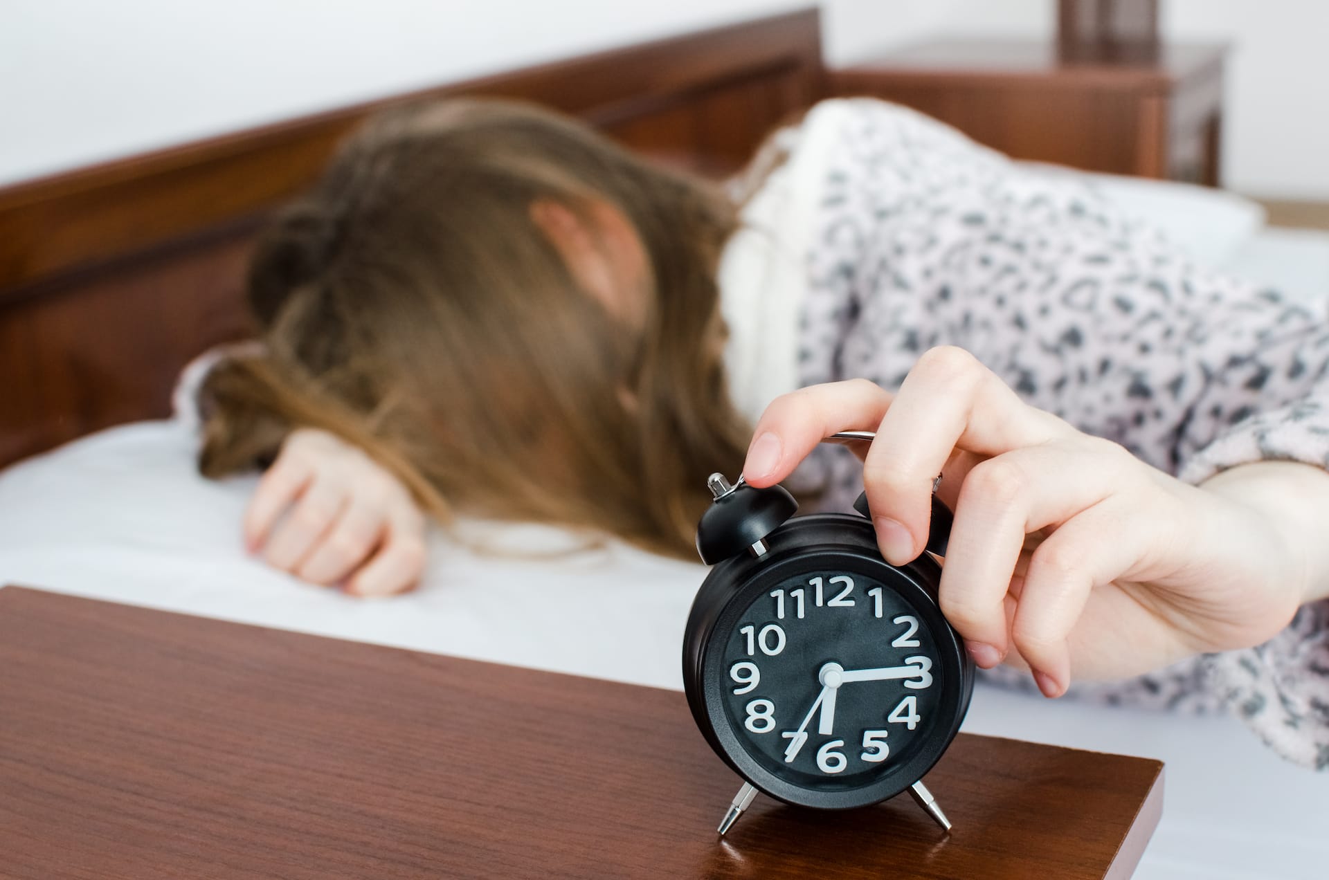 A woman face down in bed with alarm clock going off