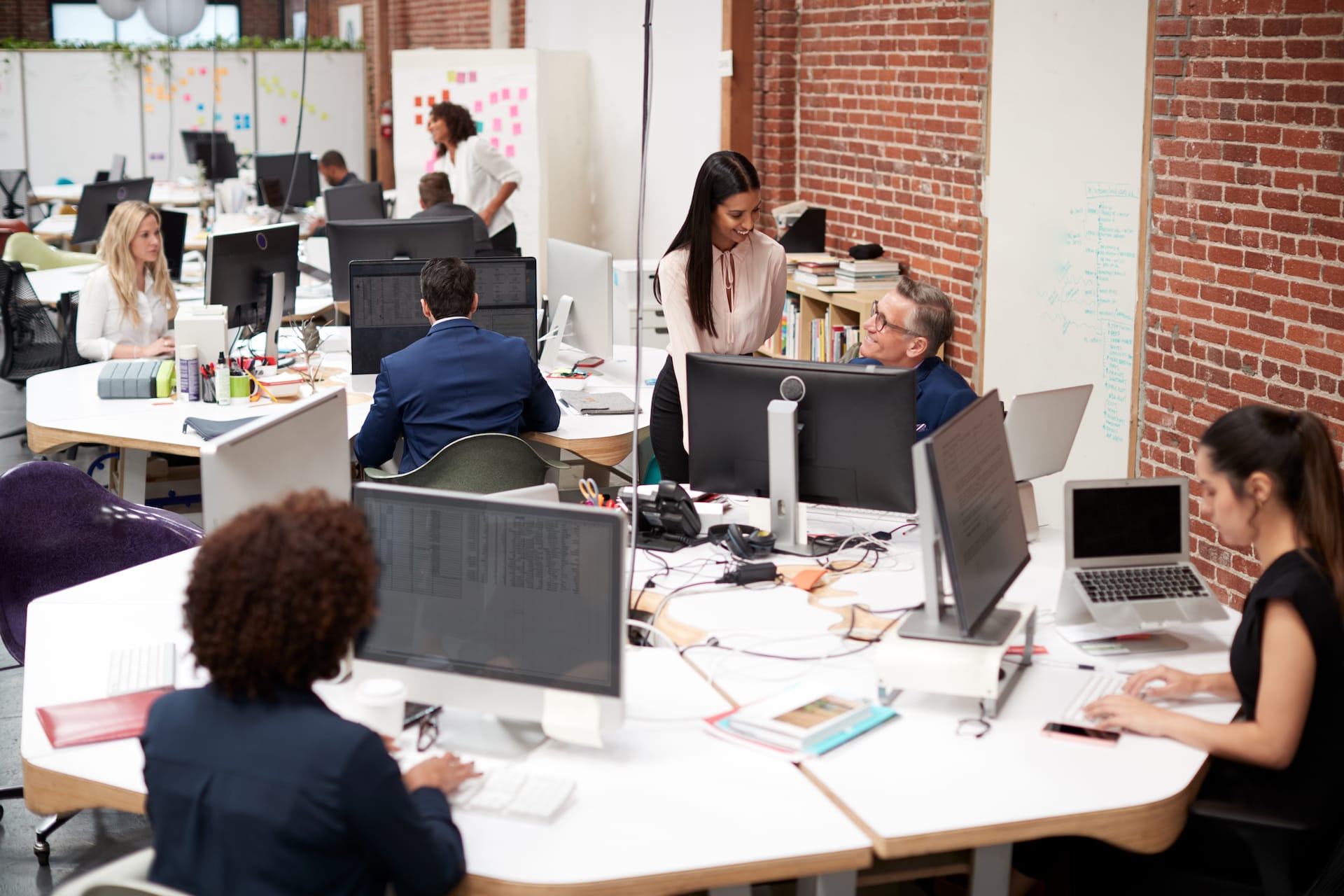 A team meeting around a desk with computers and paperwork.