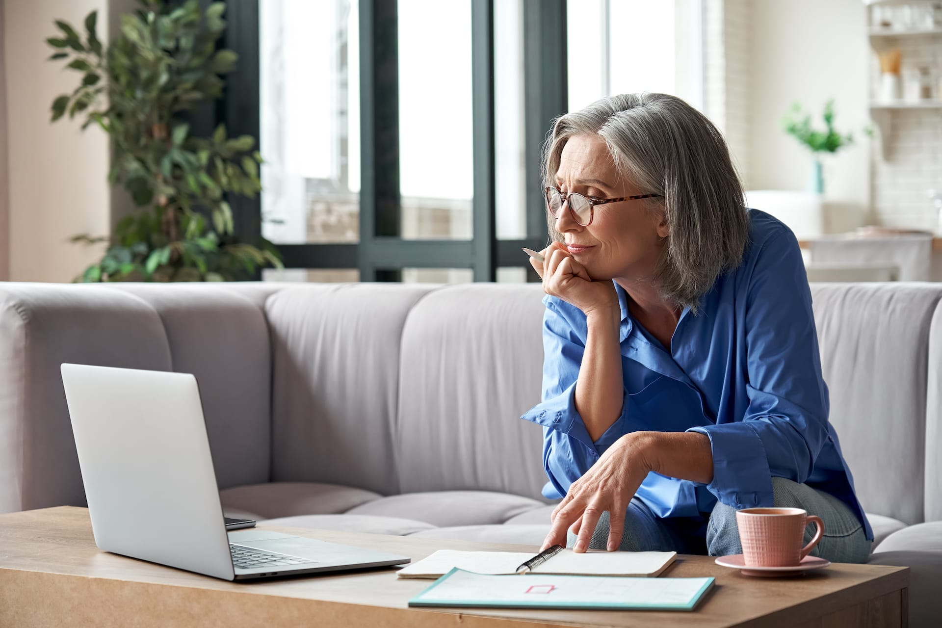 An older woman working from her couch with a laptop.